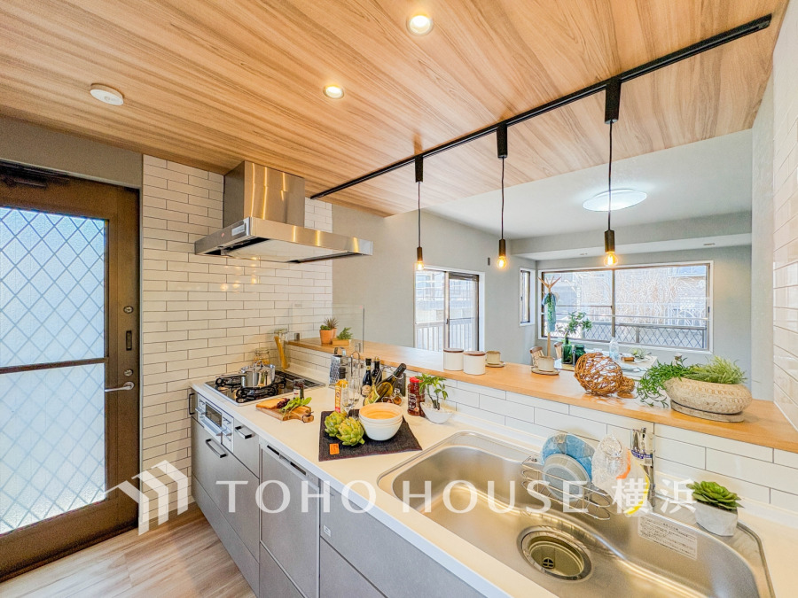 木目天井と白タイルが調和する開放的な対面キッチンで、家族との会話も弾む明るい空間です。