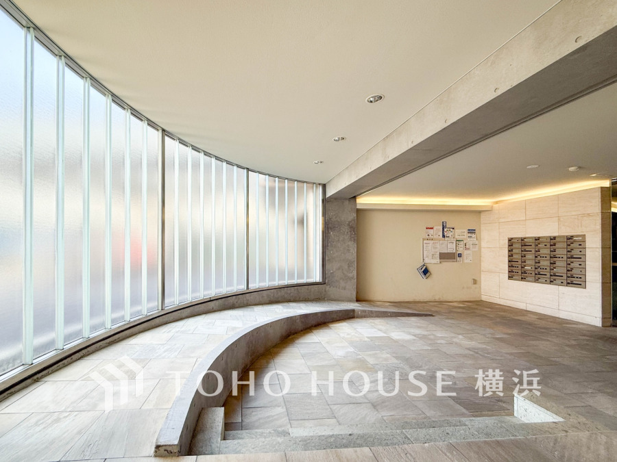 曲線ガラス壁が印象的なエントランスホール。柔らかな自然光が差し込む落ち着いた空間です。