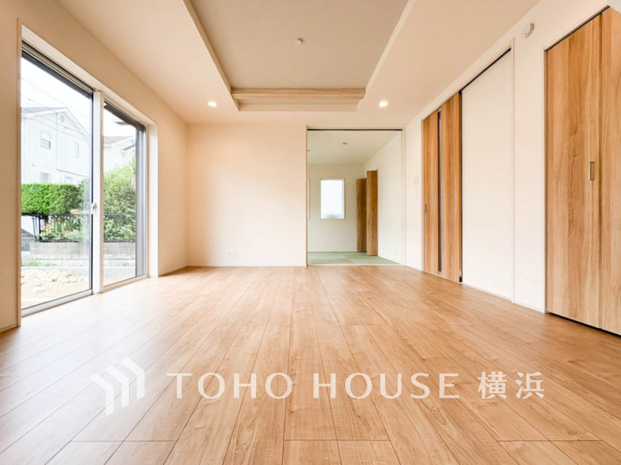 大きな窓から自然光が差し込む、木目調の床が温かみを演出する明るいリビング空間です。